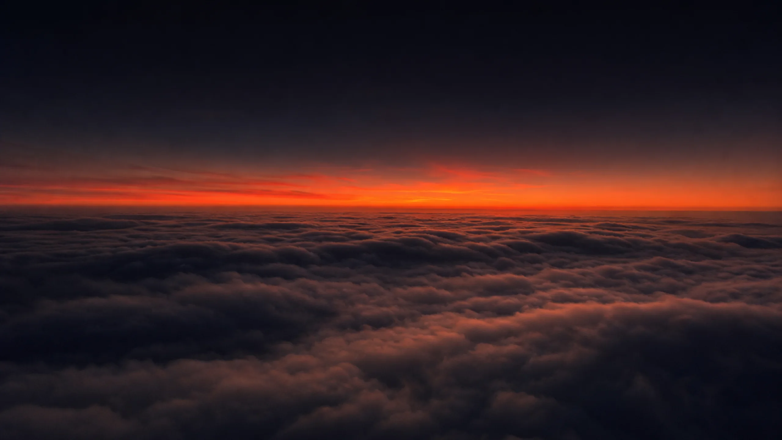 Dawn light breaks in orange and coral behind a layer of clouds seen from above