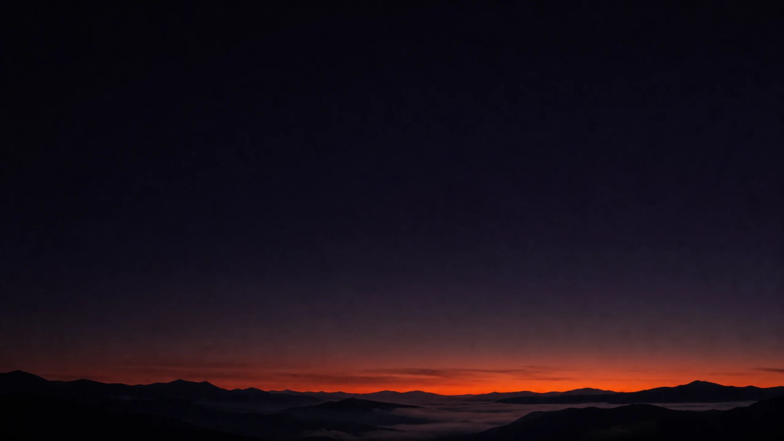 A dark mountain ridge at dusk under a vast ink sky, a thin band of ember light hugging the ridgeline