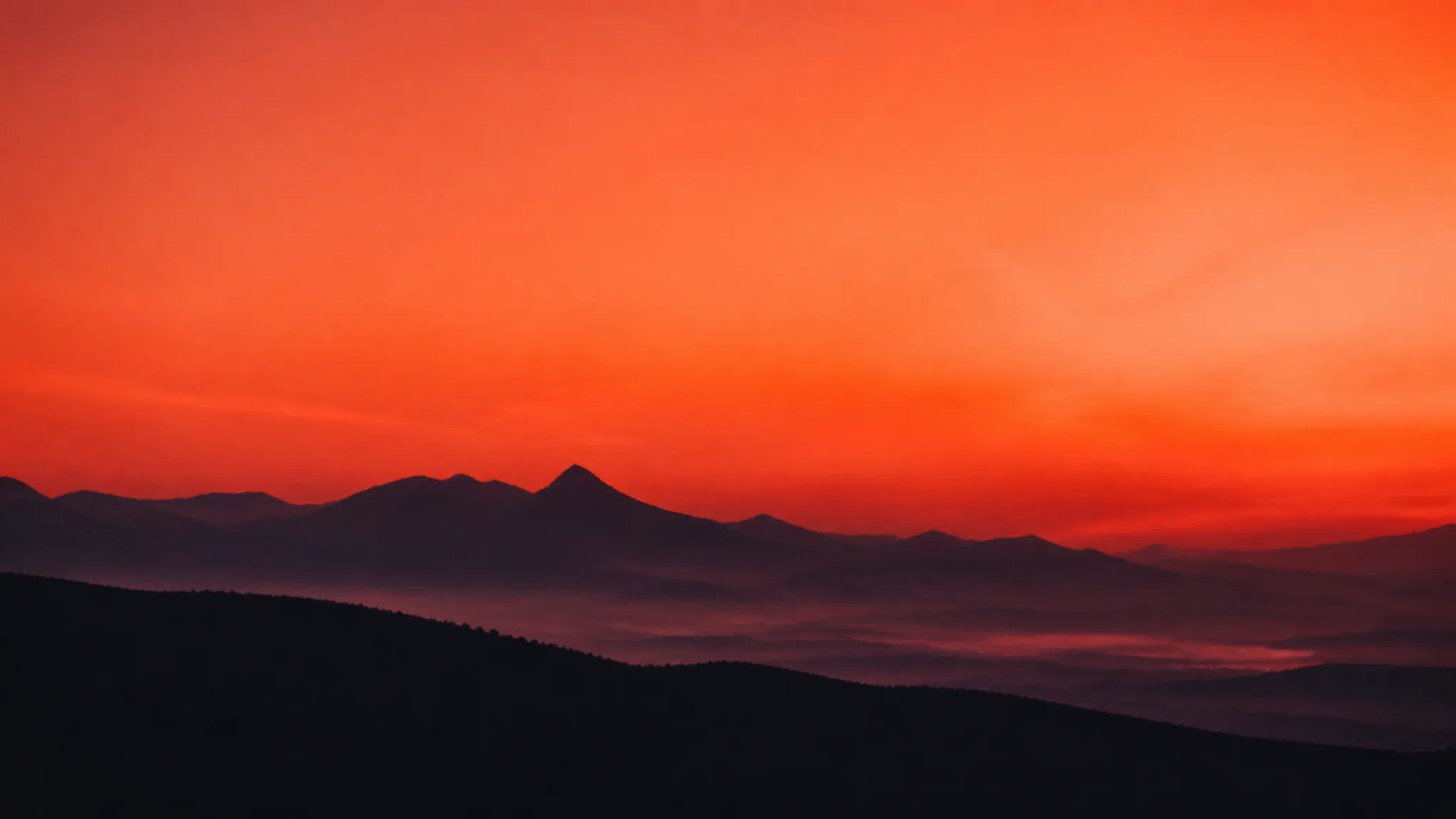 A dark mountain ridge under a sky burning with ember dusk light