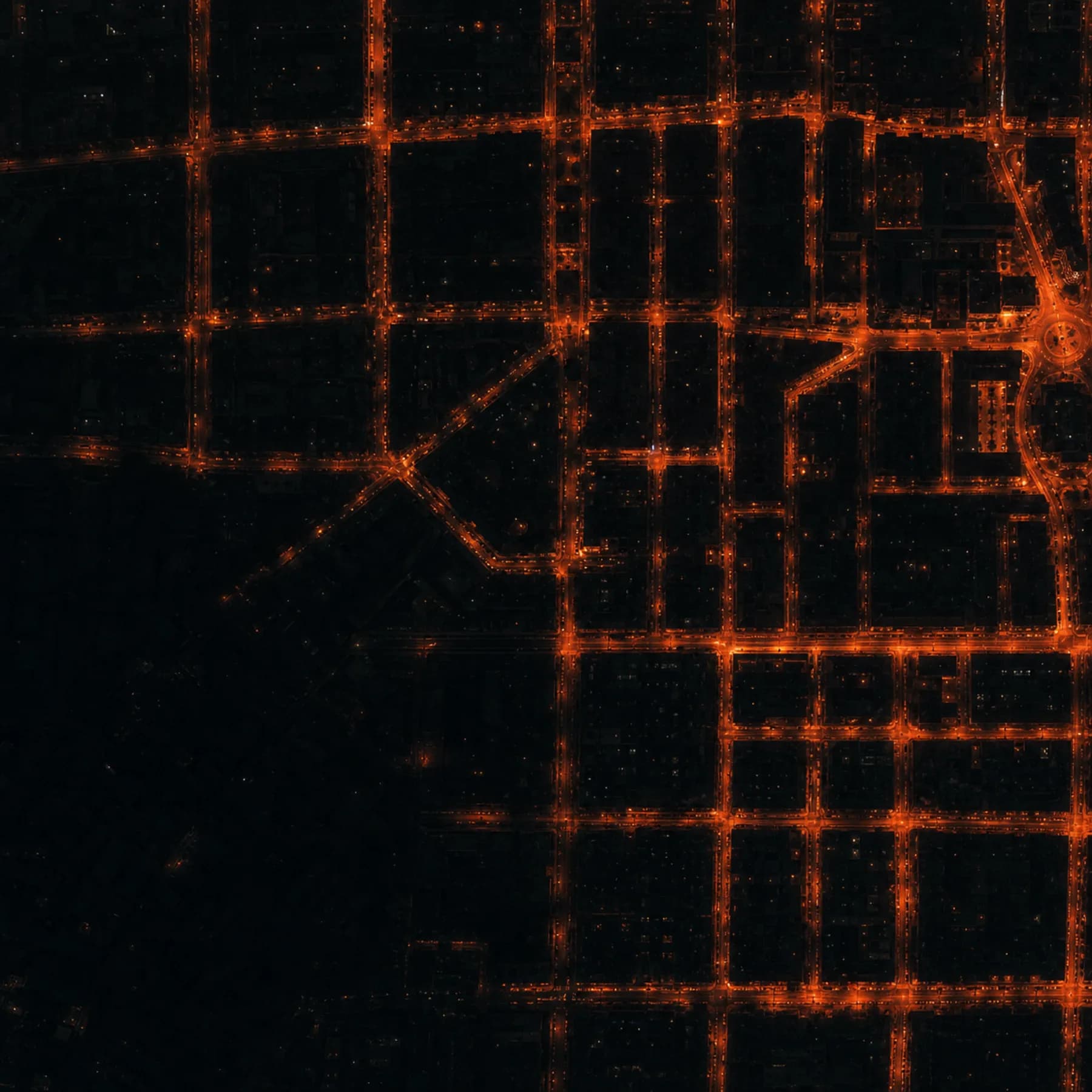 A city street grid at night from above, streetlights tracing warm orange lines through the dark.